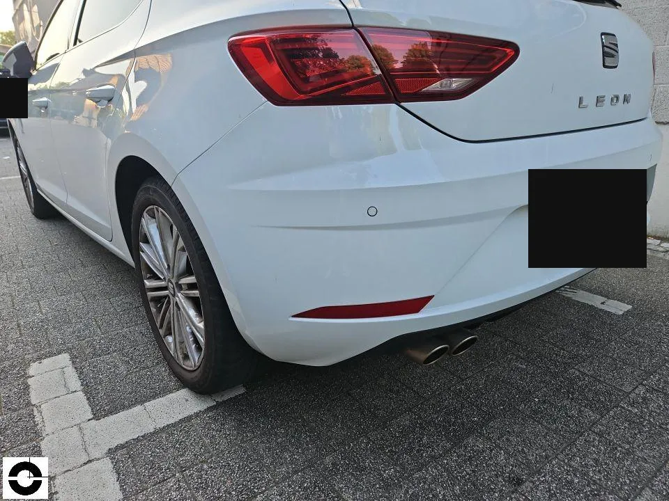 Heck eines weißen Pkw mit erneuertem Stoßfänger auf einem Parkplatz, Kennzeichen geschwärzt