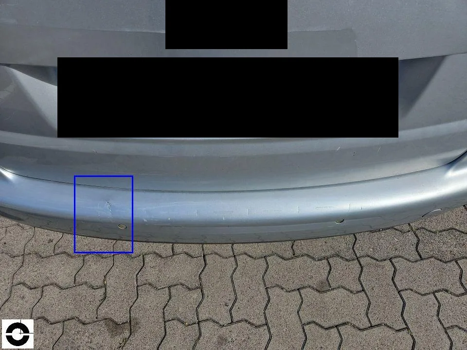 Heck eines silbernen VW Touran, ein blauer Rahmen markiert einen älteren Kratz- und Dellenschaden am hinteren Stoßfänger, Kennzeichen geschwärzt