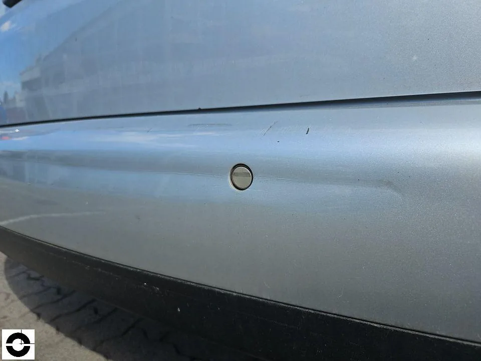 Nahaufnahme eines silbernen hinteren Stoßfängers mit waagerechter Eindrückung und Kratzern rund um einen Parksensor