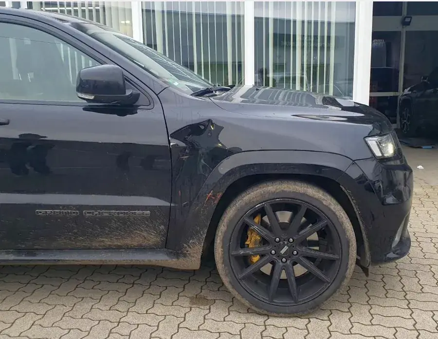 Dunkler SUV (Jeep Grand Cherokee) mit Front- und Felgenschaden